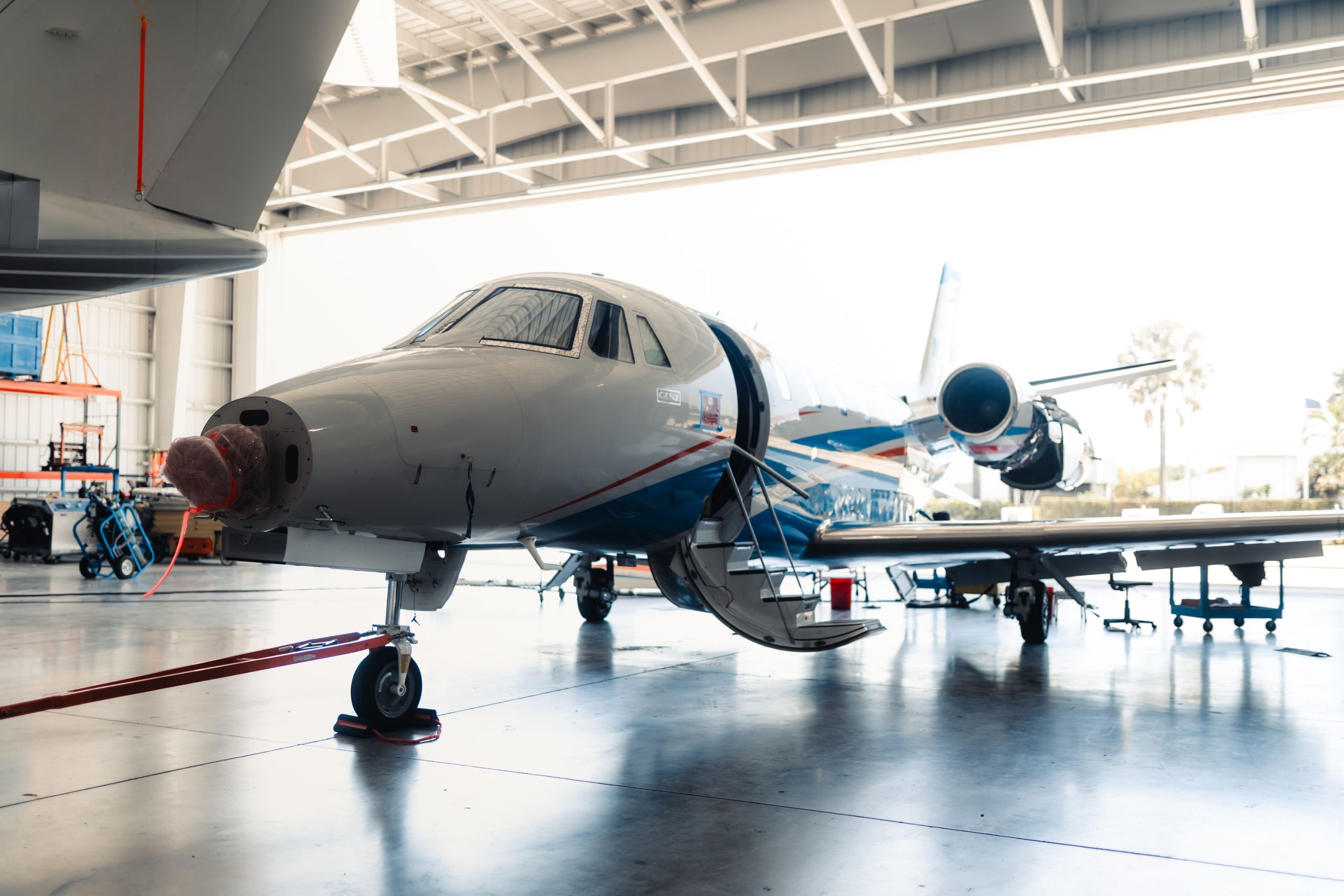 A business jet on jacks inside a Fly Alliance hangar, doors open to the ramp